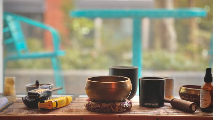 An altar with a brass singing bowl in the center. There is a blurry courtyard in the background.